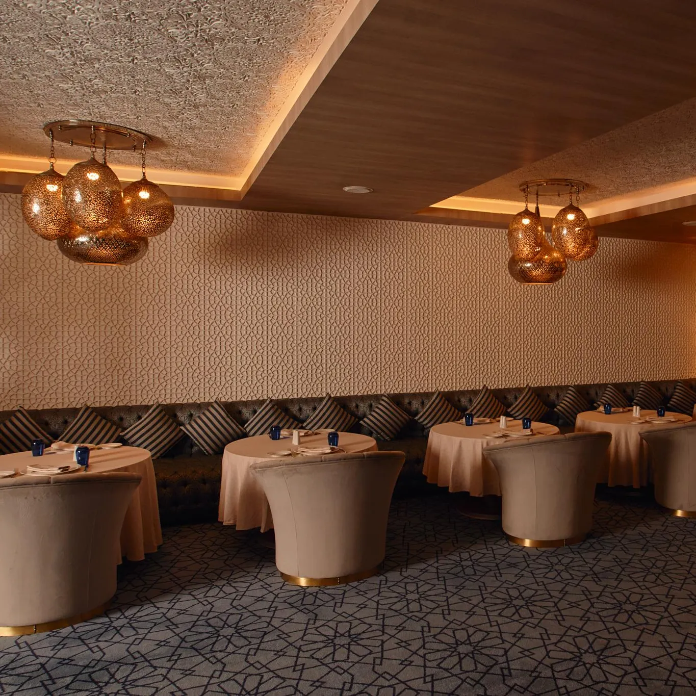 Salle de restaurant élégante avec tables rondes recouvertes de nappes beige, banquettes et luminaires suspendus