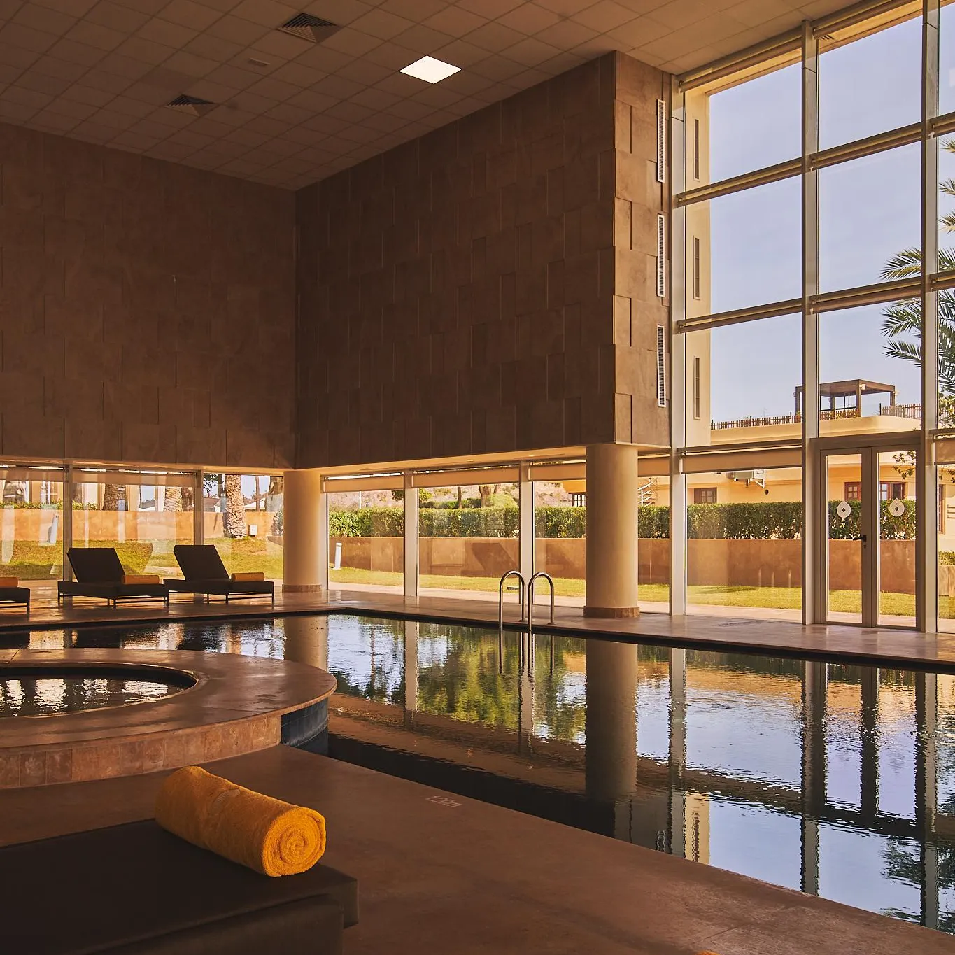 Piscine intérieure avec des transats et des serviettes, entourée de grandes fenêtres et de murs en pierre