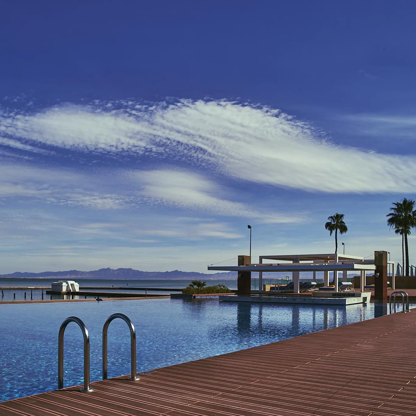 Piscine à débordement avec vue sur un lac et des montagnes sous un ciel bleu avec quelques nuages