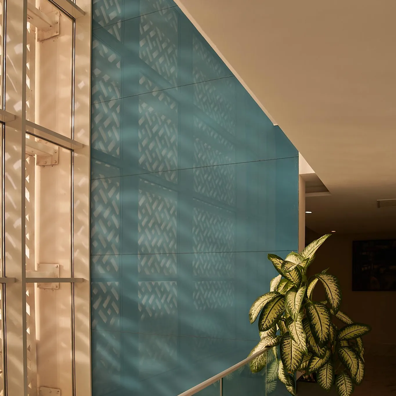 Mur bleu avec motif géométrique et plante verte en pot près d'une rambarde et d'une fenêtre