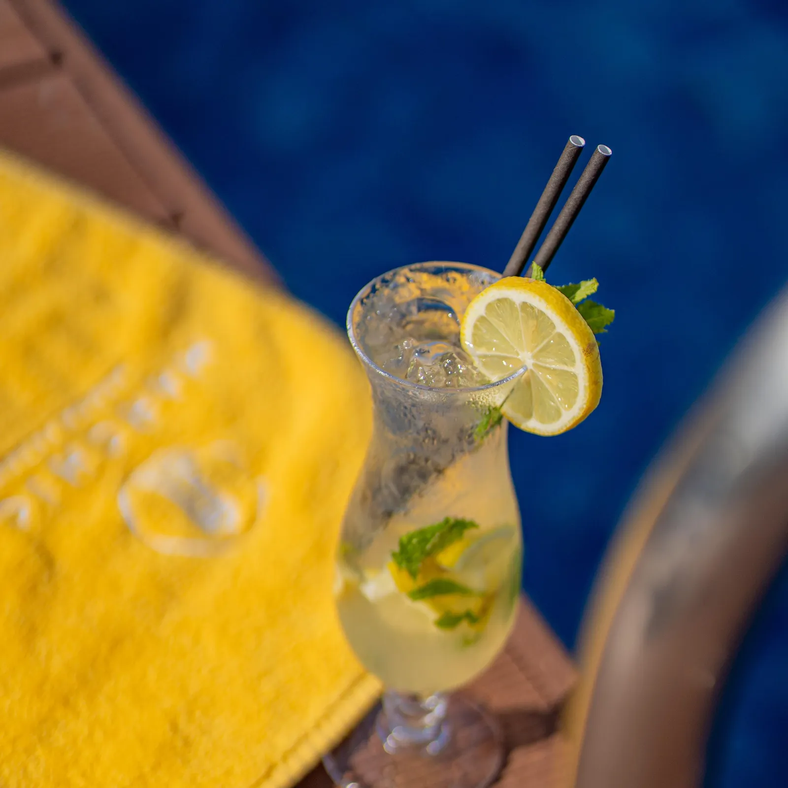 Un verre de boisson fraîche avec une tranche de citron et des feuilles de menthe, posé sur une table en bois à côté d'une serviette jaune
