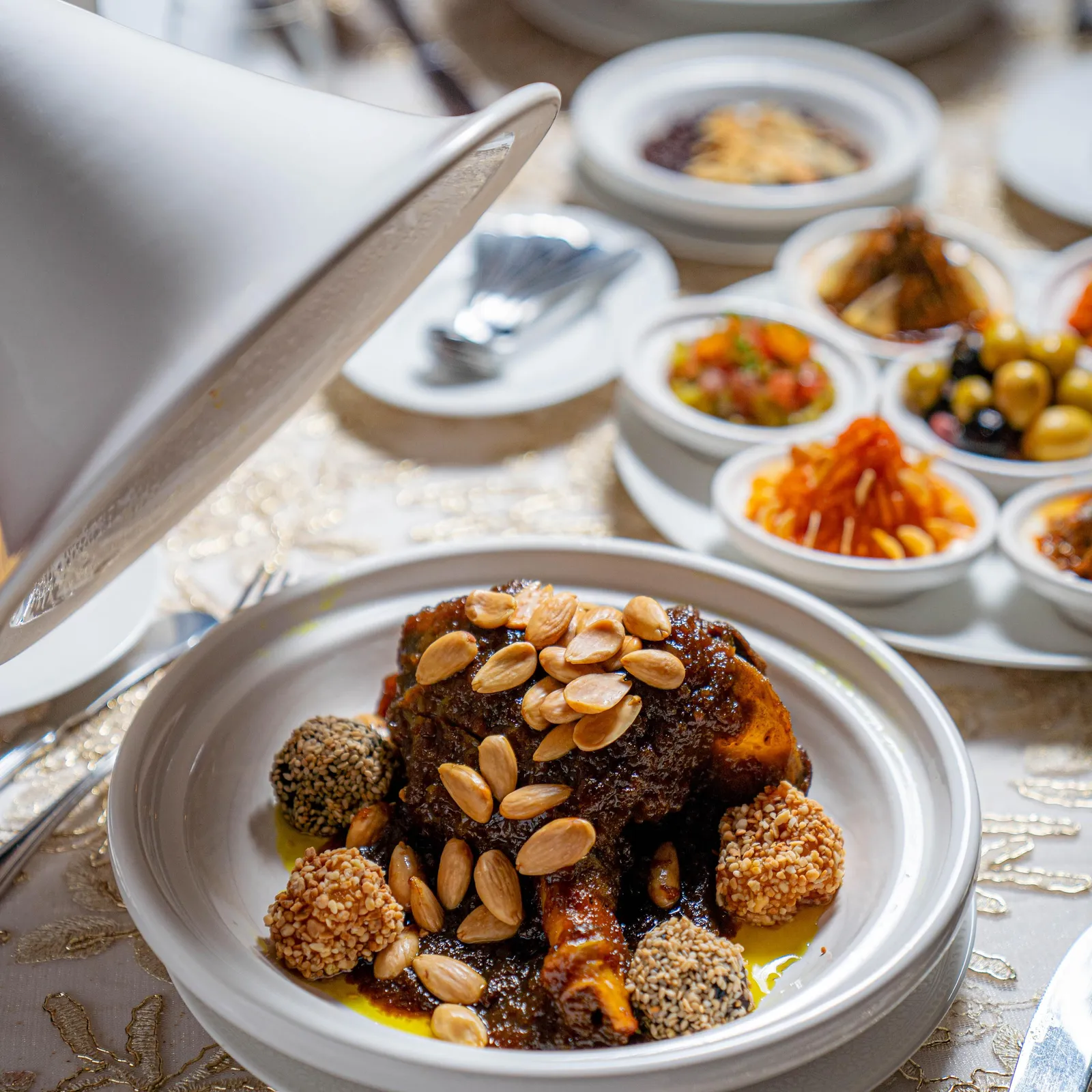 Un plat de viande garnie de graines de sésame et d'amandes, entouré de plusieurs petits bols de différentes préparations culinaires
