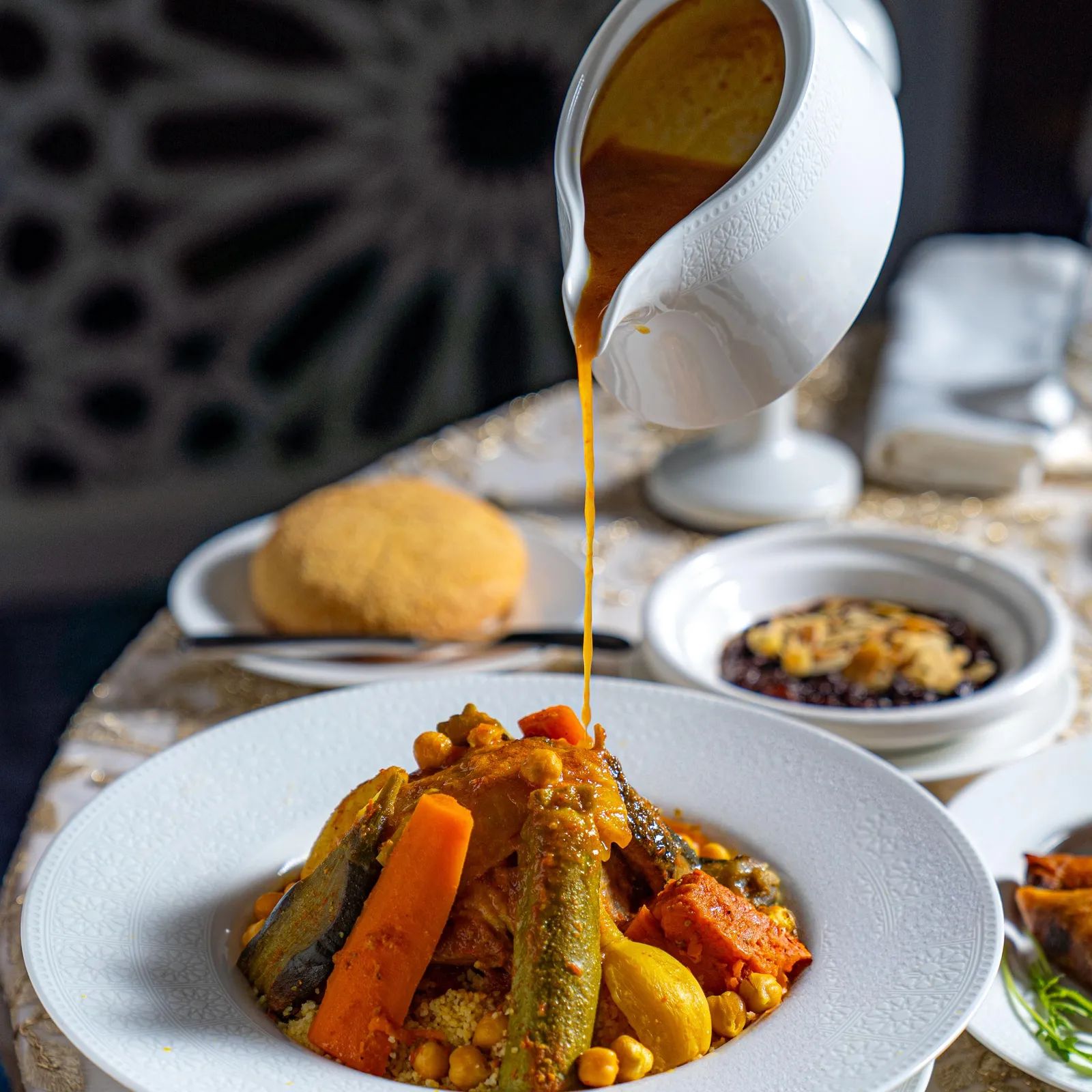 Une main verse une sauce à partir d'une louche sur un plat contenant des légumes et des pois chiches