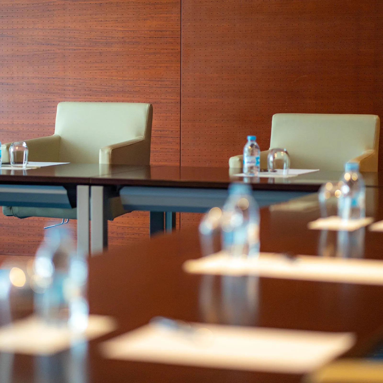 Une rangée de tables de conférence avec des bouteilles d'eau et des verres devant des chaises vides dans une salle aux murs en bois