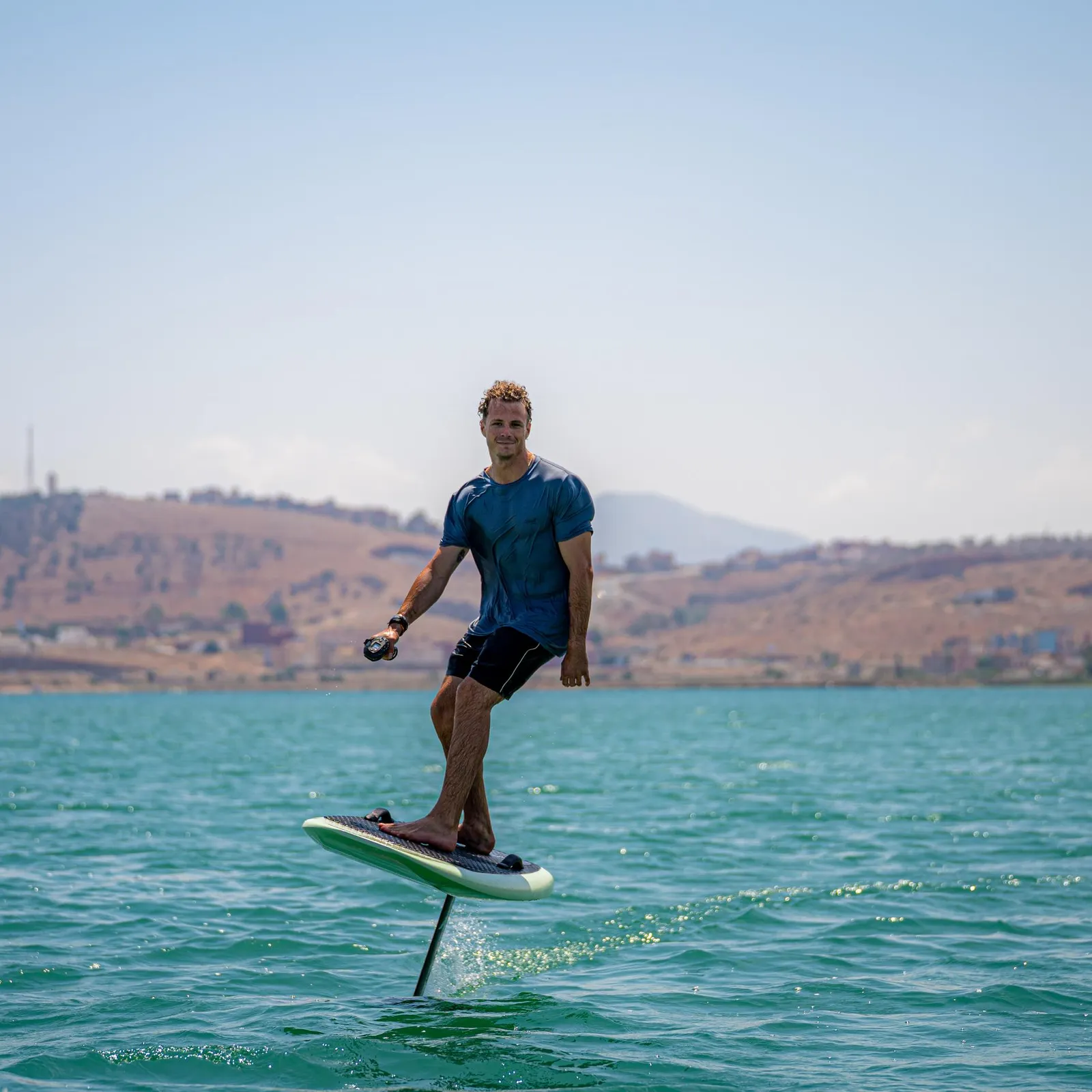 Un homme debout sur une planche de paddle dans une étendue d'eau avec des collines en arrière-plan