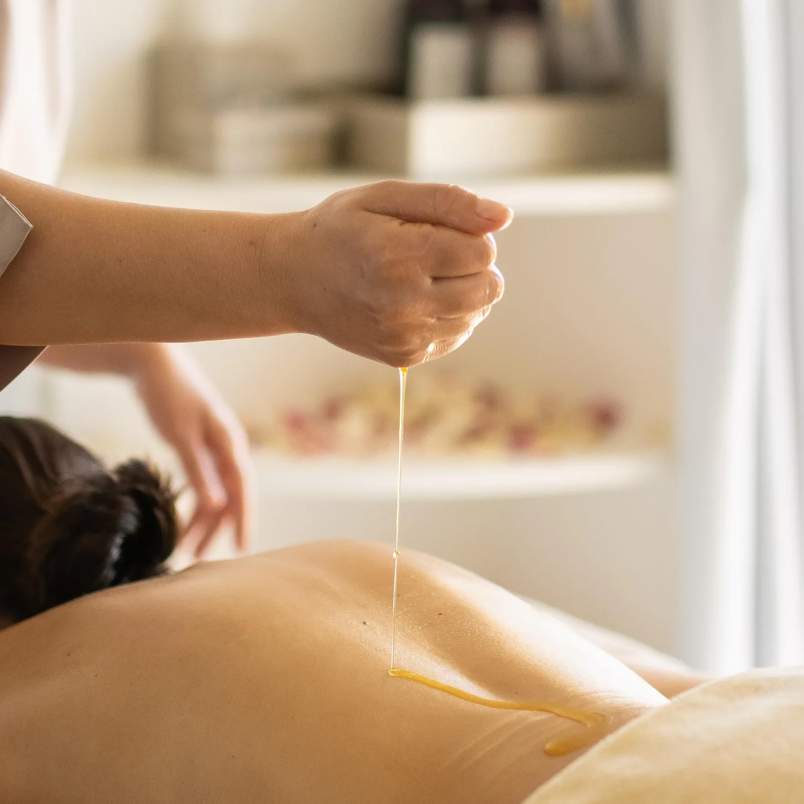 Une personne verse un liquide sur le dos d'une personne allongée sur une table de massage