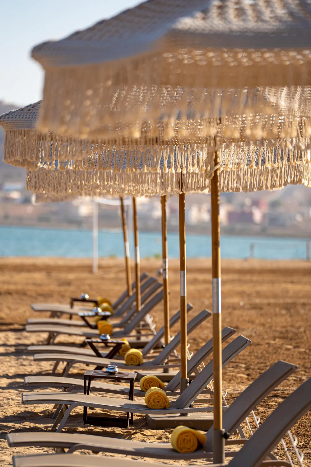 Une rangée de transats avec des serviettes jaunes sous des parasols en paille sur une plage au bord de l'eau