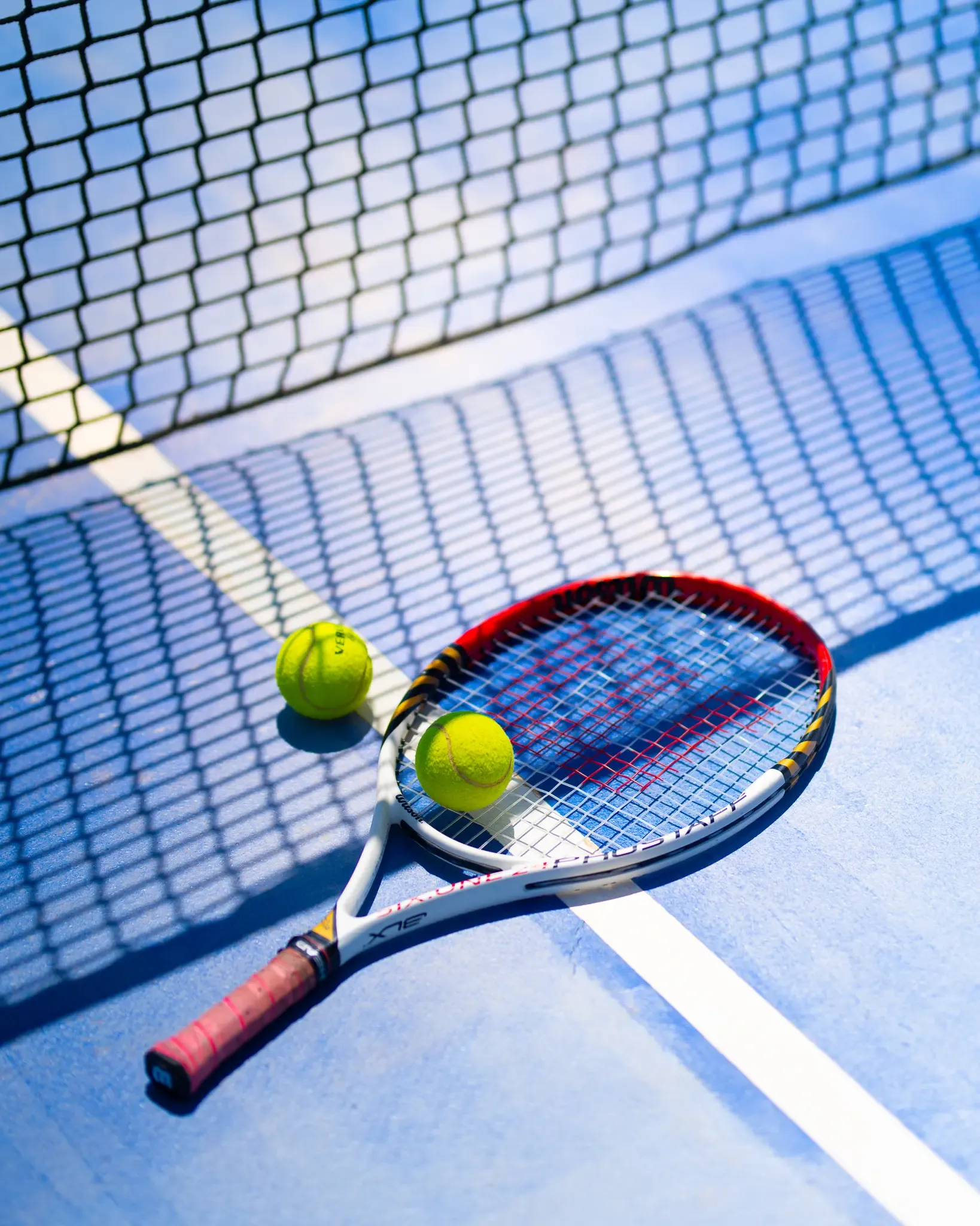 Raquette de tennis avec deux balles sur un court près du filet