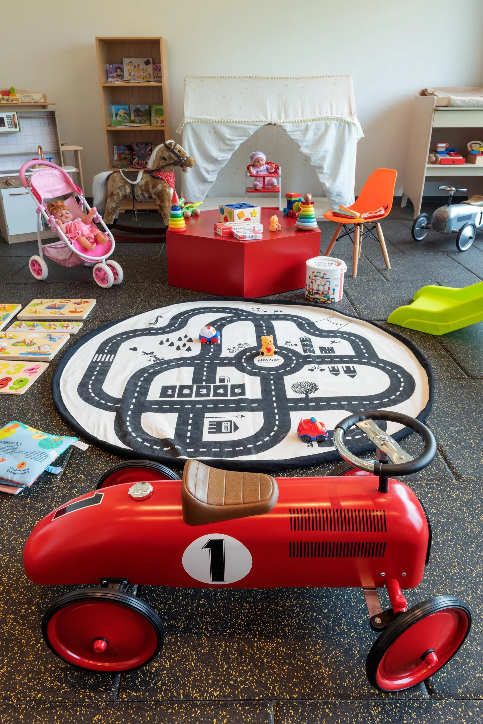 Chambre d'enfant avec jouets, dont une voiture rouge, un tapis de route et un cheval à bascule