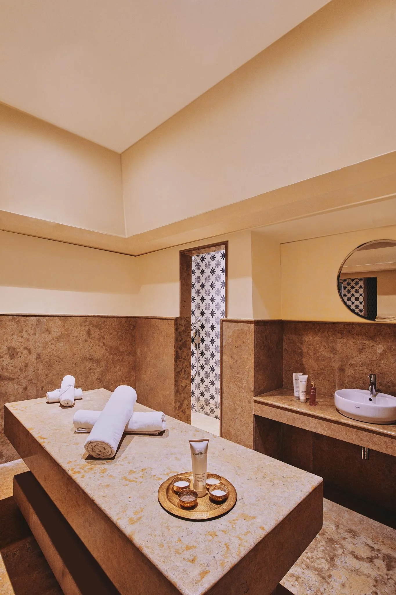 Salle de massage avec table de soins, serviettes, produits et lavabo dans un cadre aux murs en pierre et éclairage tamisé