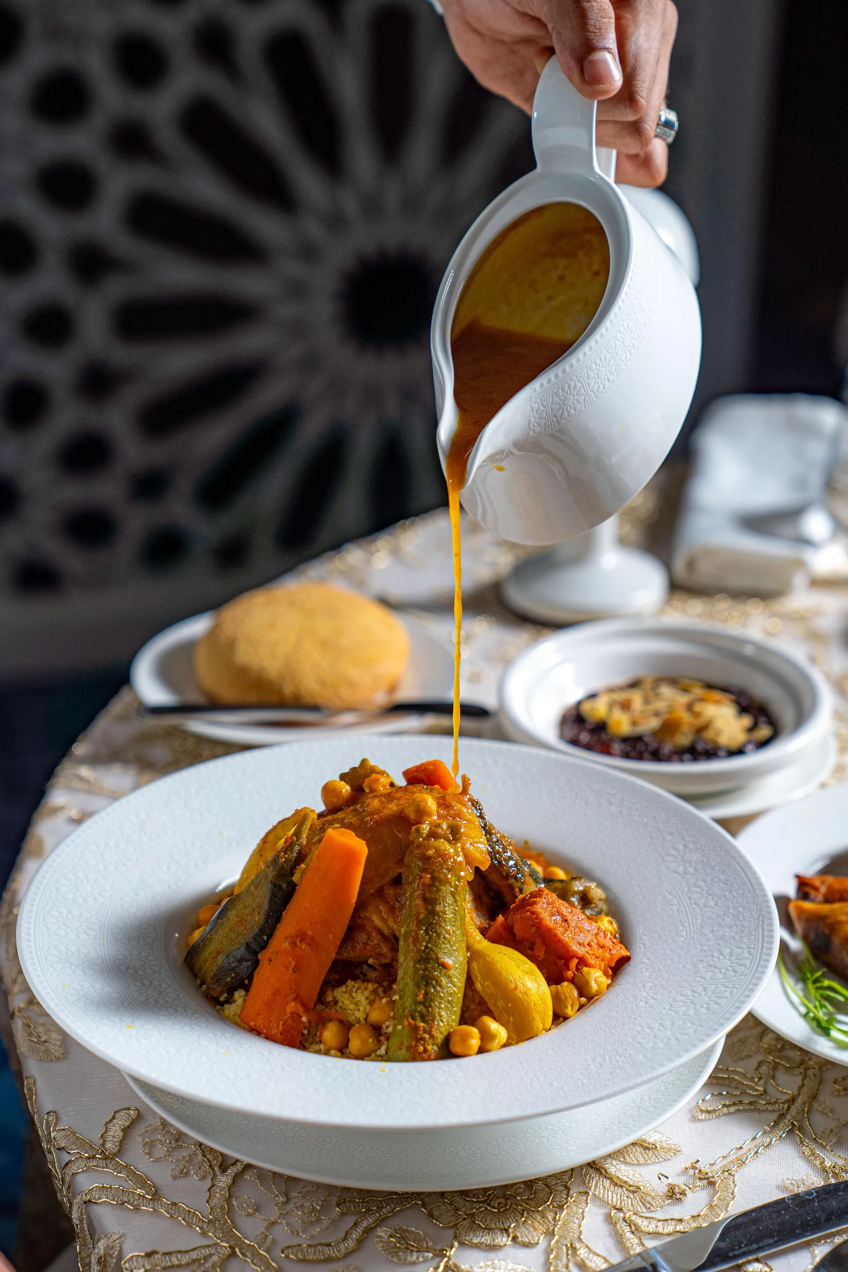 Une main verse une sauce à partir d'une louche sur un plat contenant des légumes et des pois chiches