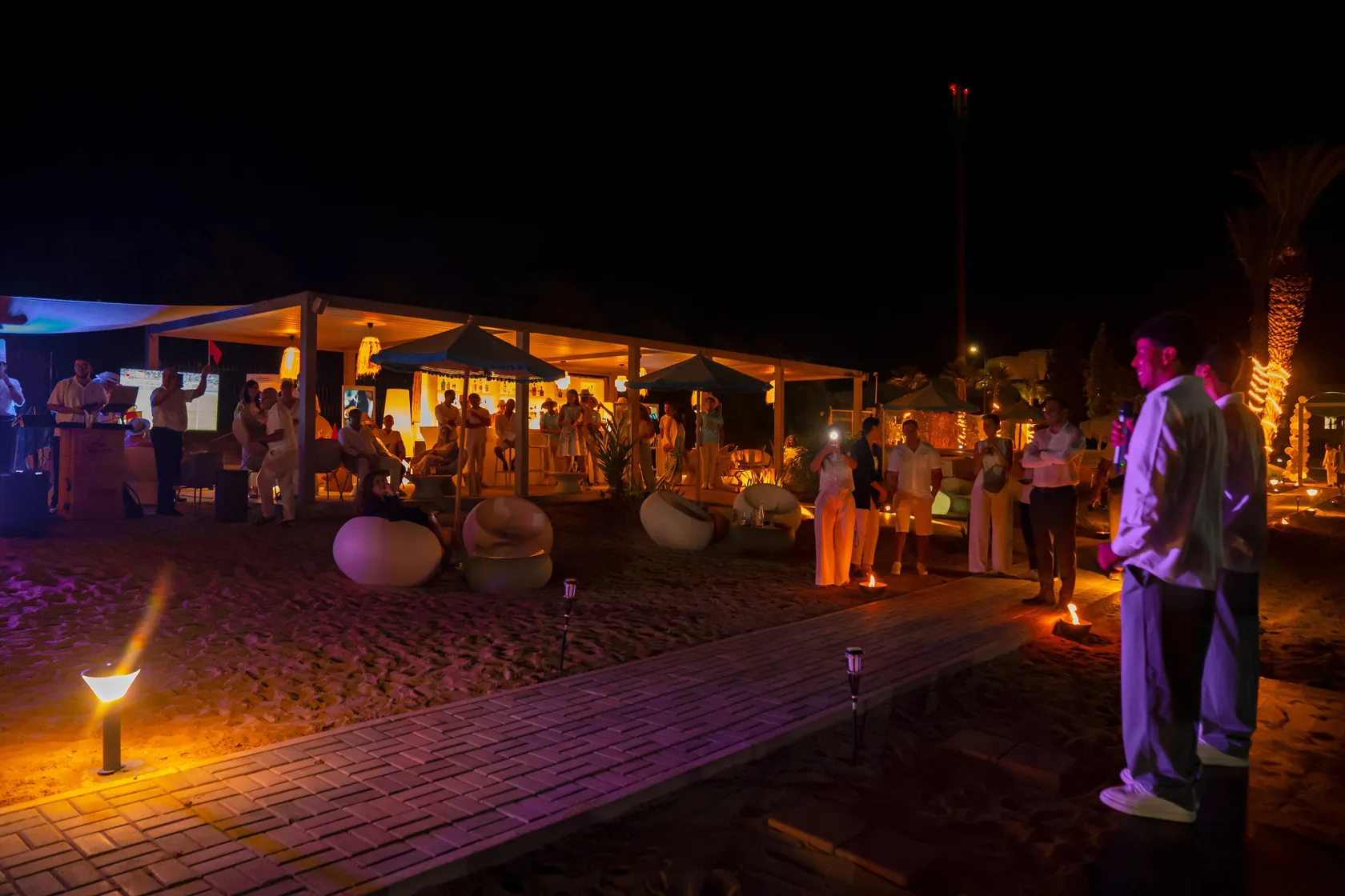 Un groupe de personnes se tient autour d'une structure éclairée sur une plage de nuit