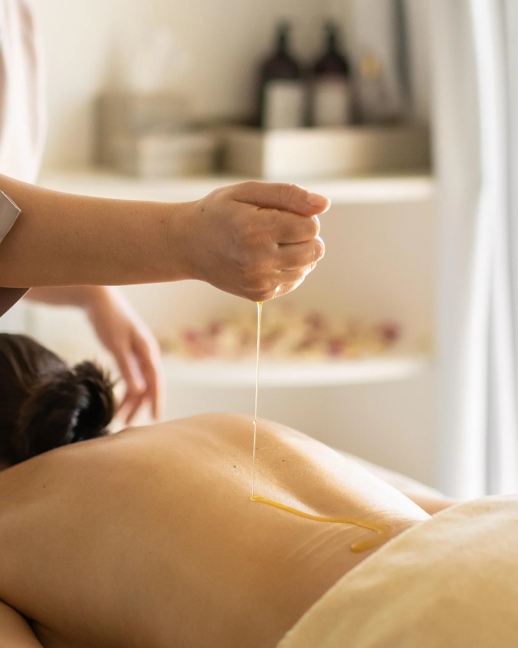 Une personne verse un liquide sur le dos d'une personne allongée sur une table de massage