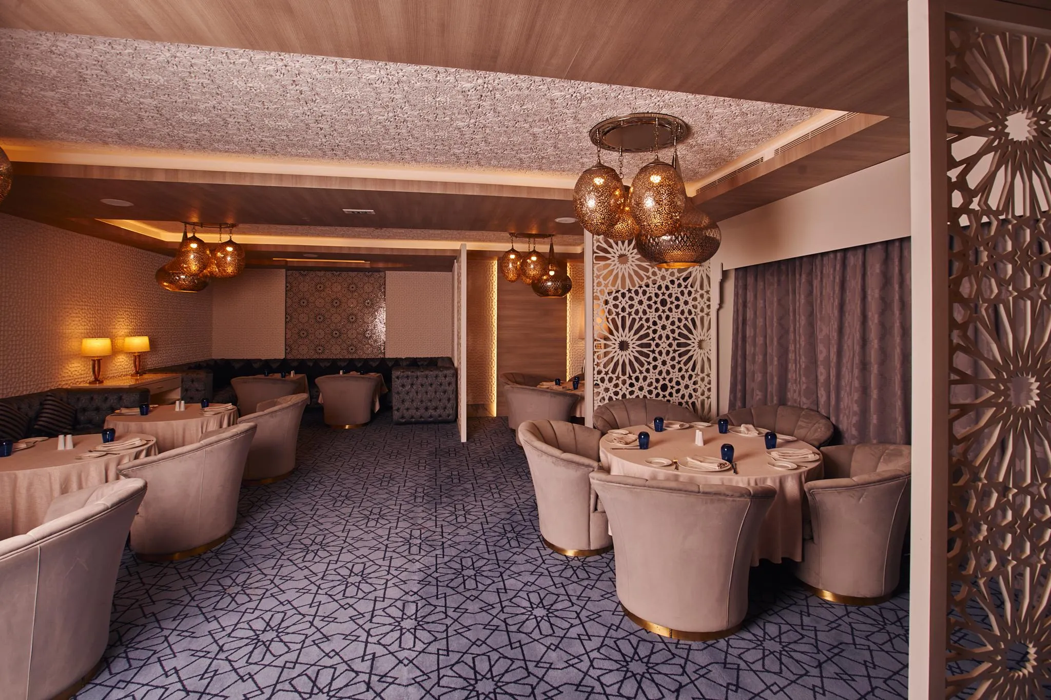 Salle de restaurant élégante avec des tables rondes, des chaises rembourrées en velours rose et des luminaires suspendus