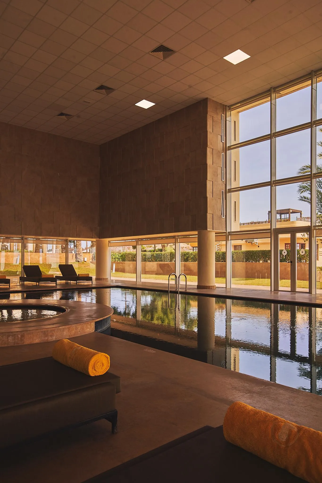 Piscine intérieure avec des transats et des serviettes, entourée de grandes fenêtres et de murs en pierre
