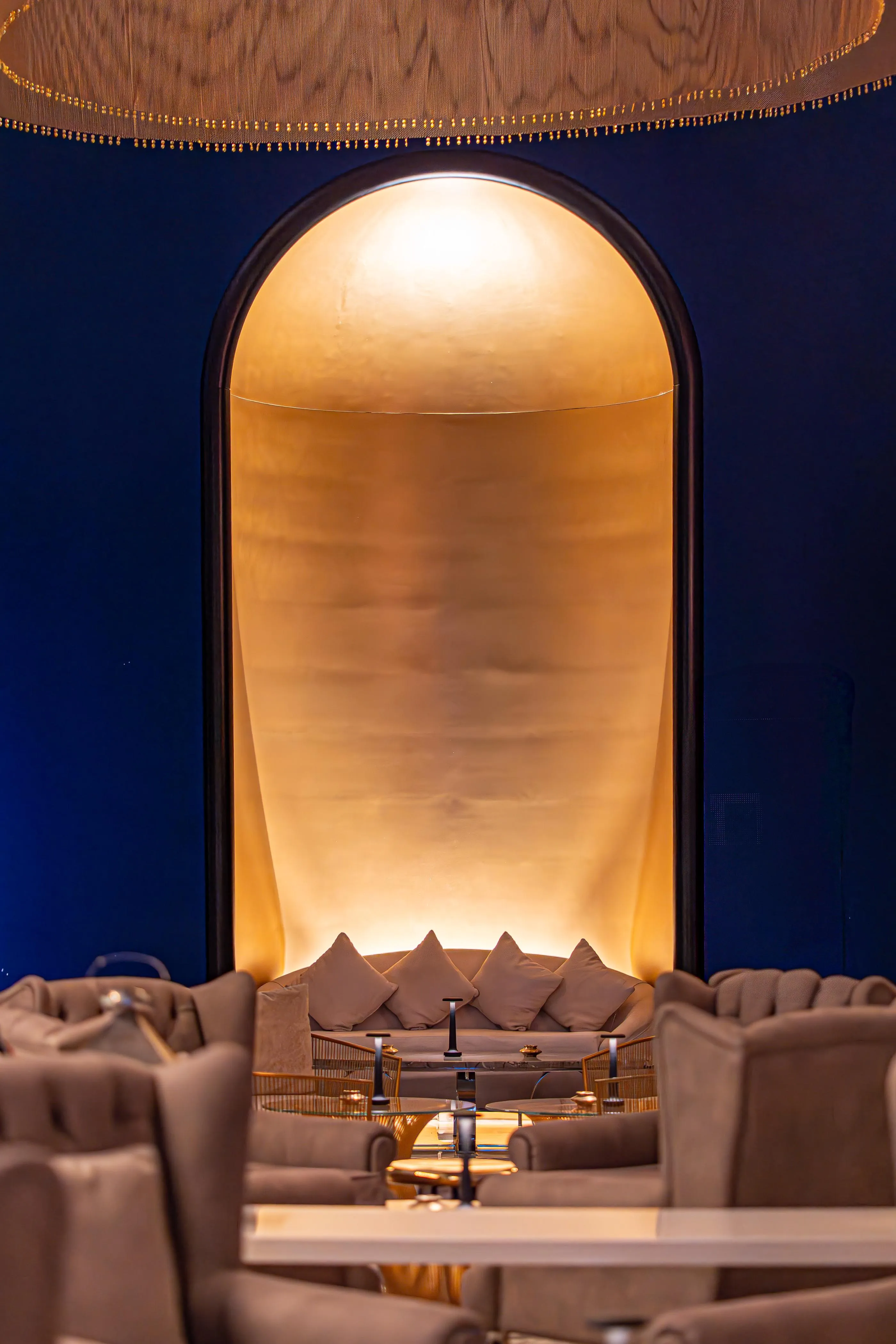 Un espace intérieur avec des canapés et une table basse, éclairé par une lumière dorée à travers une arche.