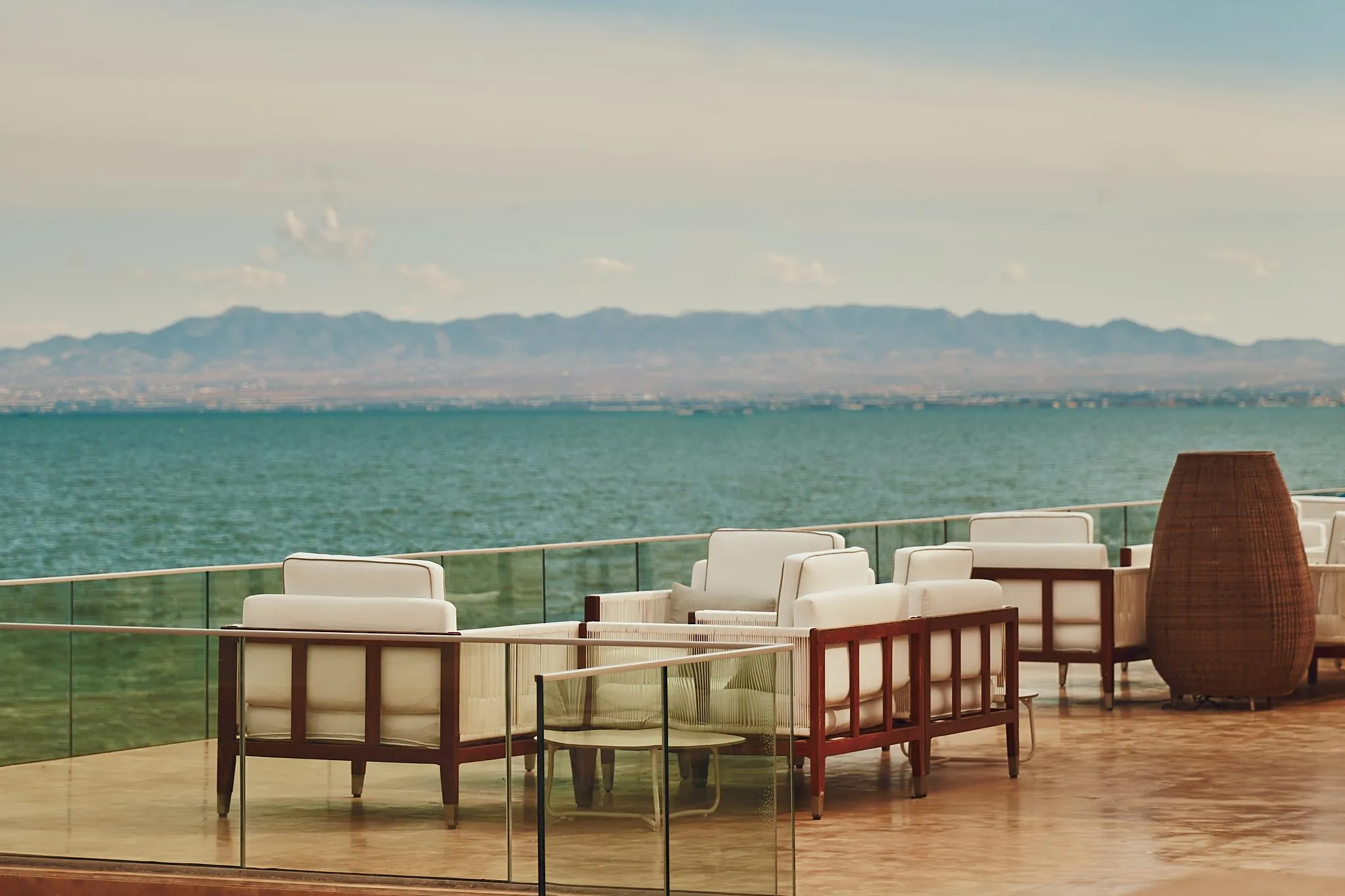 Terrasse avec des chaises et des tables face à une mer et des montagnes à l'horizon