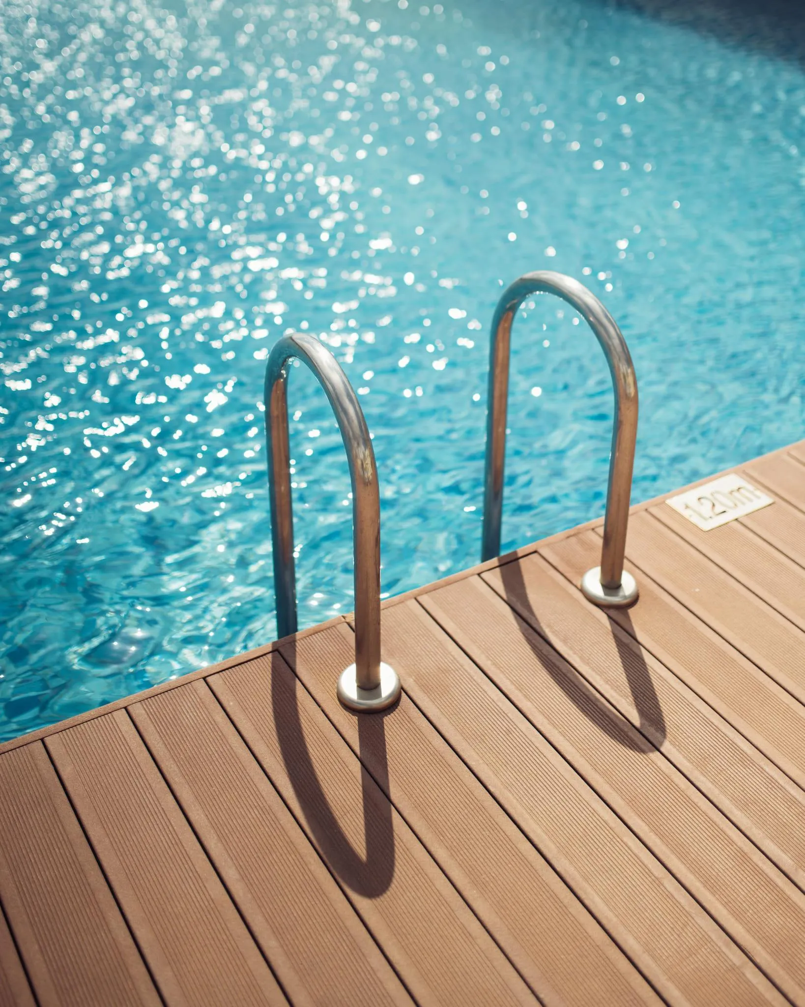 Deux barres métalliques courbées fixées sur un plancher en bois près d'une piscine remplie d'eau bleue