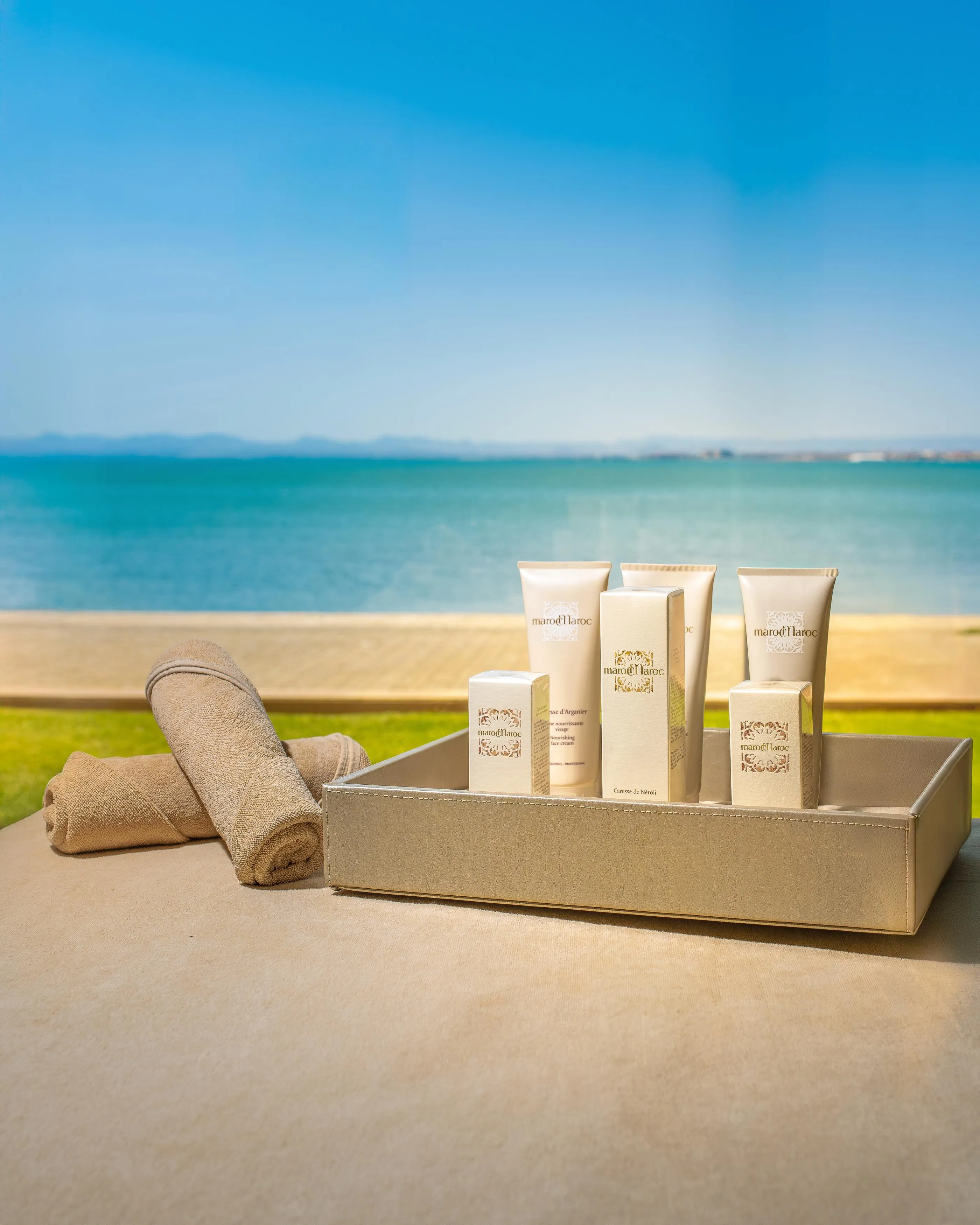 Un plateau avec des produits cosmétiques et des serviettes en tissu devant une plage et la mer
