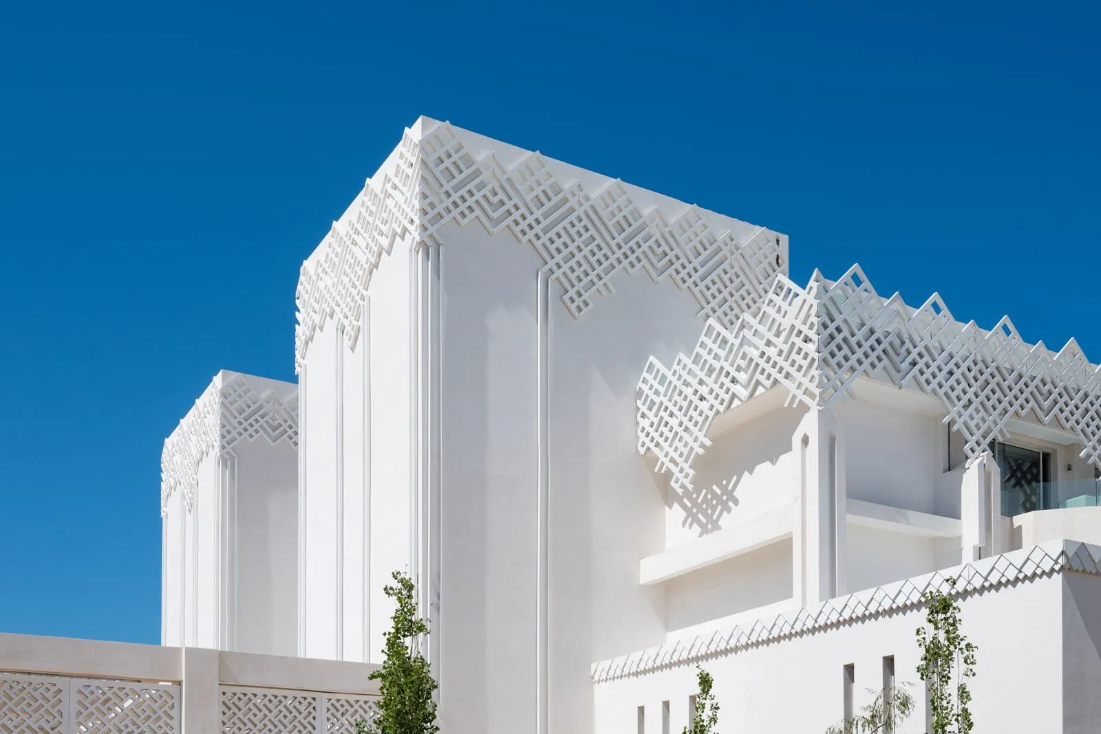 Bâtiment blanc avec des motifs géométriques en relief sur la façade et le toit, sous un ciel bleu clair