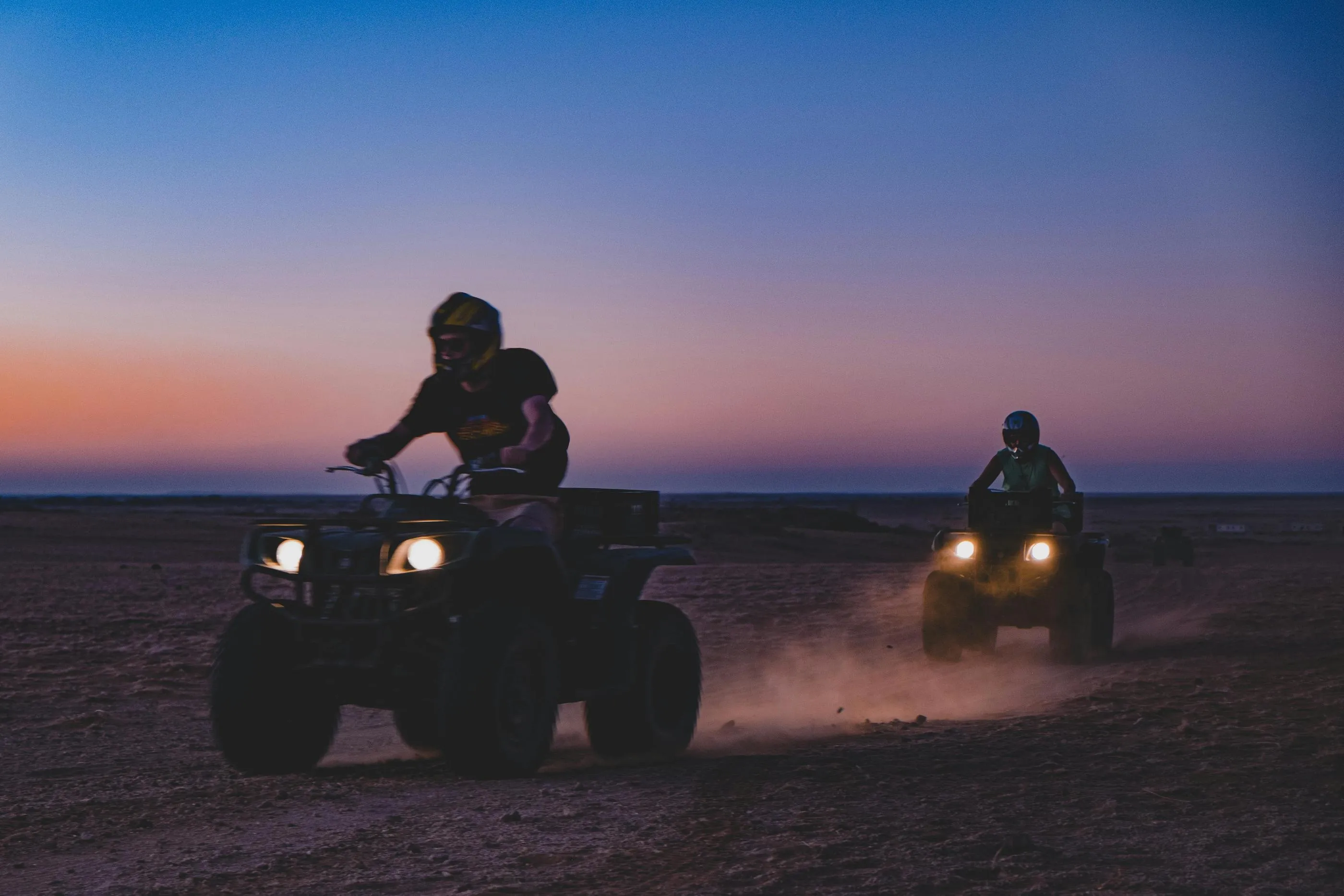 Deux personnes conduisent des quadricycles dans un désert à l'heure du coucher du soleil