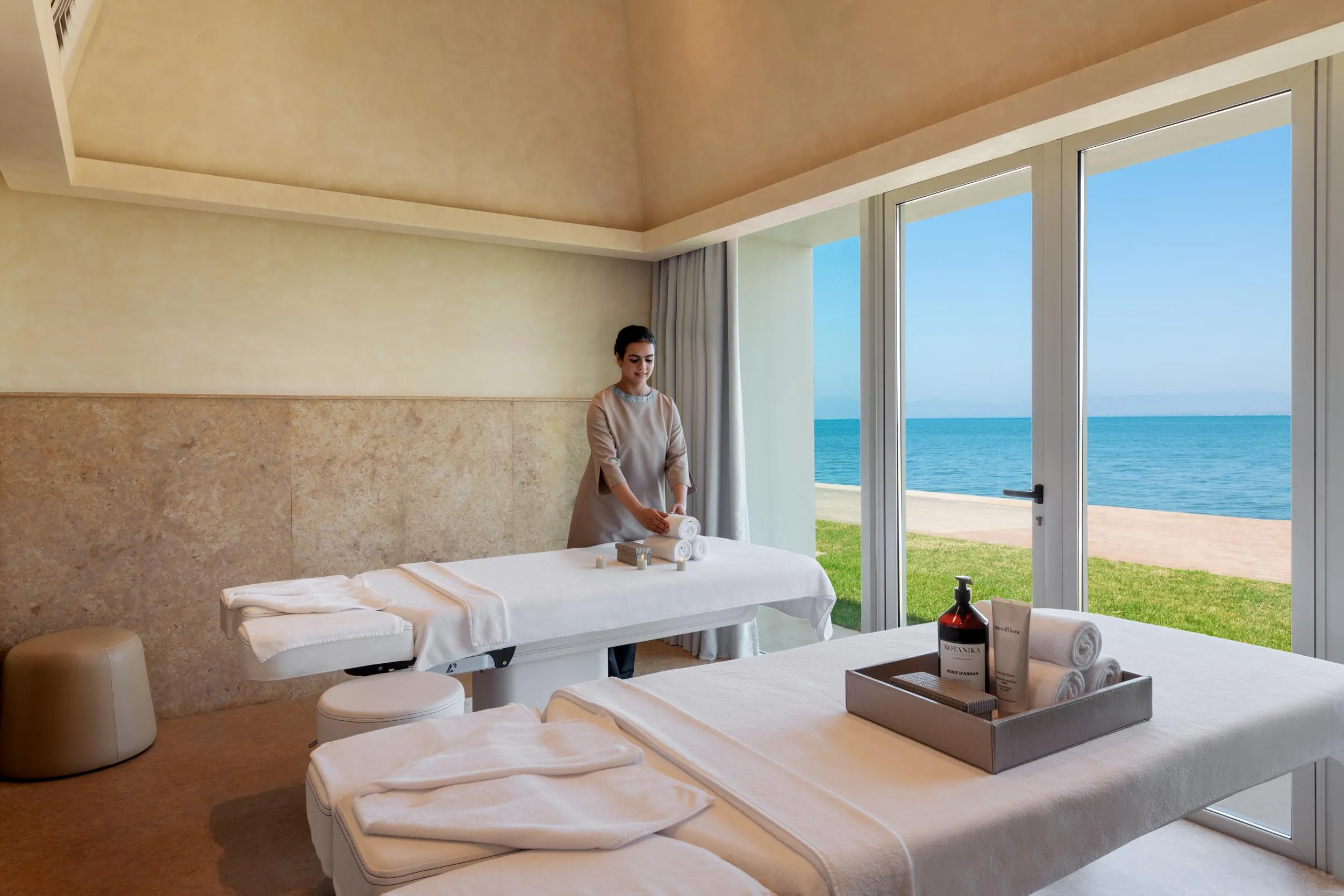 Une personne en tenue de travail prépare une table de massage dans une salle avec vue sur la mer