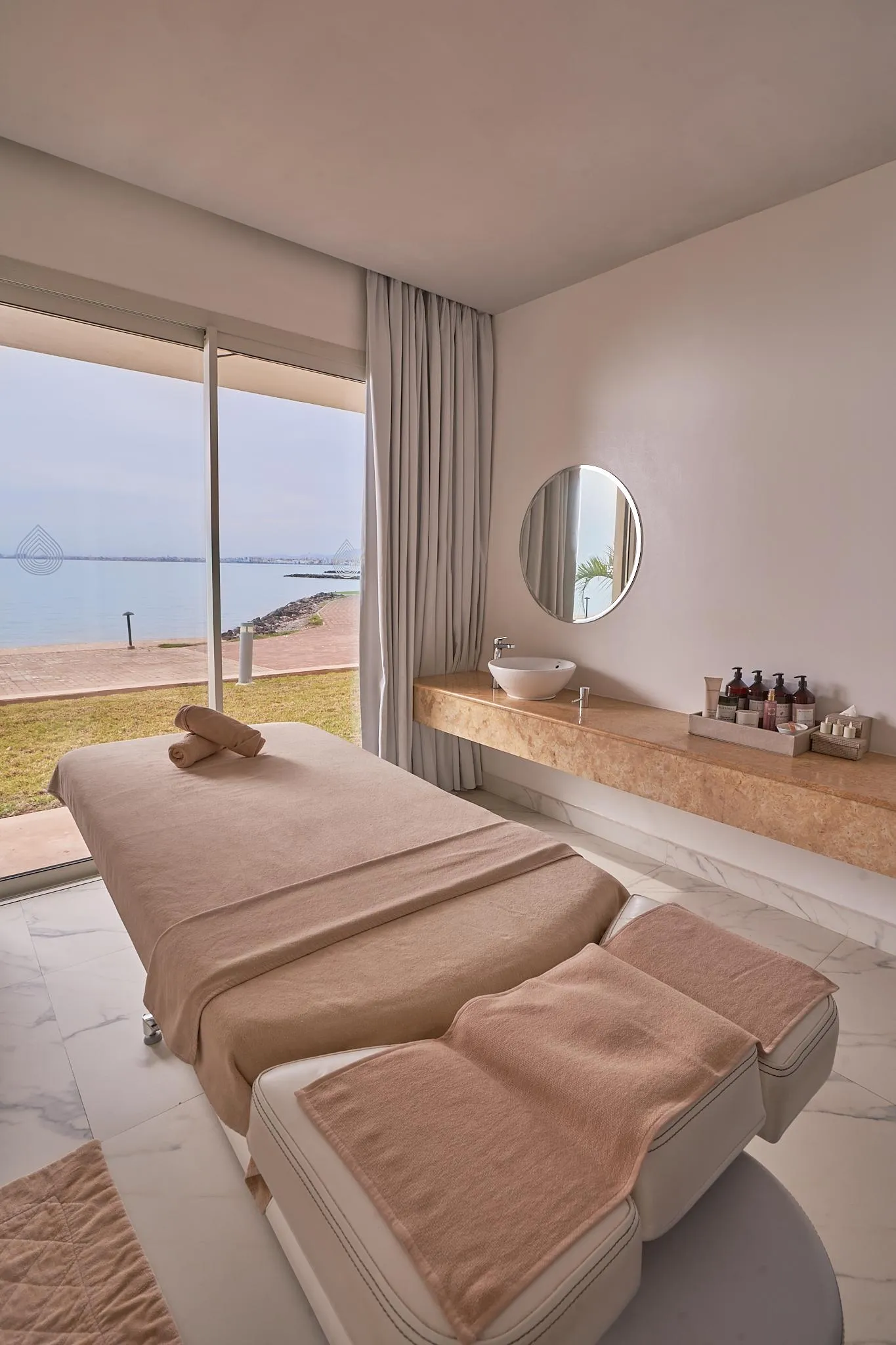 Salle de massage avec deux tables de soins, une vasque et une vue sur la mer