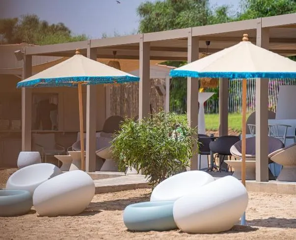 Un espace extérieur avec des canapés blancs et bleus, des parasols à franges bleues et des pergolas en bois