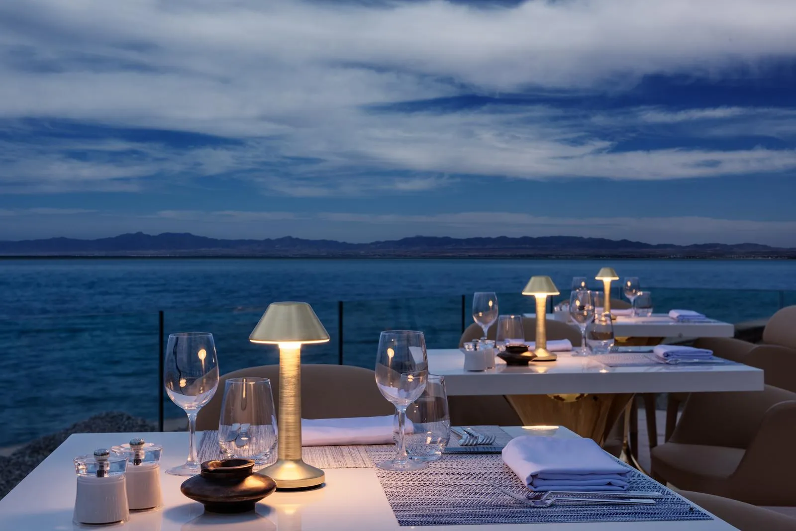 Tables dressées avec verres et bougies sur une terrasse face à la mer au coucher du soleil