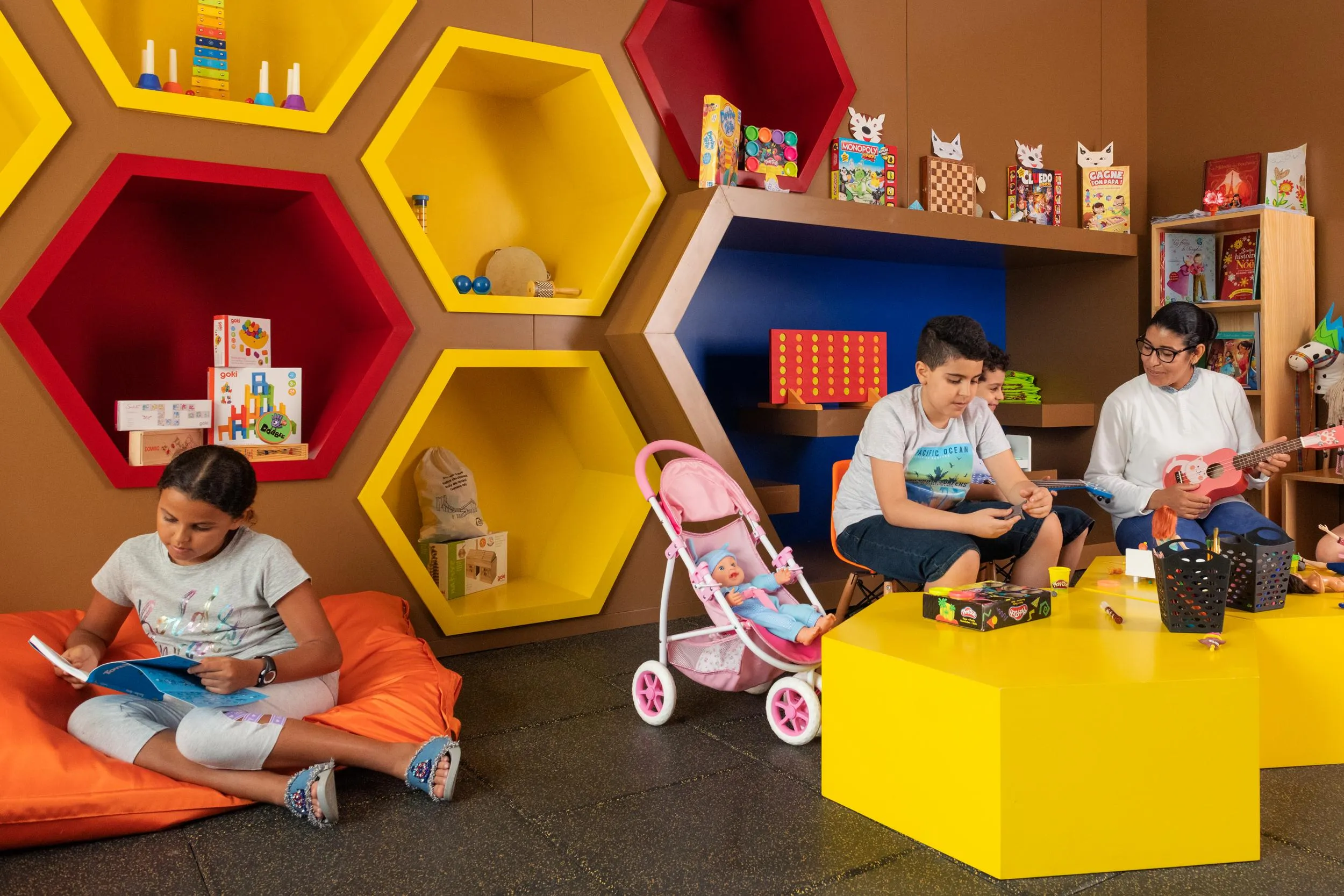 Enfants lisant et jouant dans une pièce colorée avec des étagères en forme d'hexagones remplies de jouets et de livres