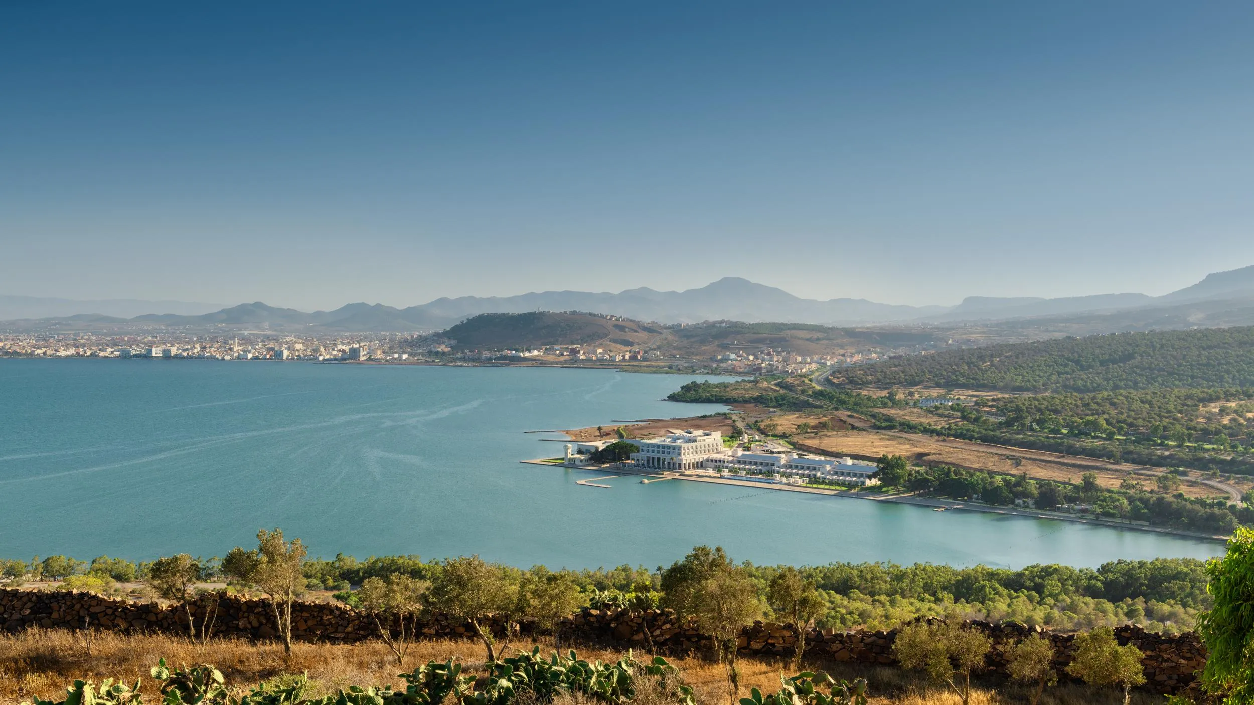 Vue panoramique d'un lac entouré de collines et de montagnes avec un bâtiment blanc en bordure de rive