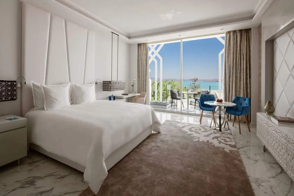Chambre d'hôtel avec lit double, table et chaises près d'une grande baie vitrée offrant une vue sur la mer