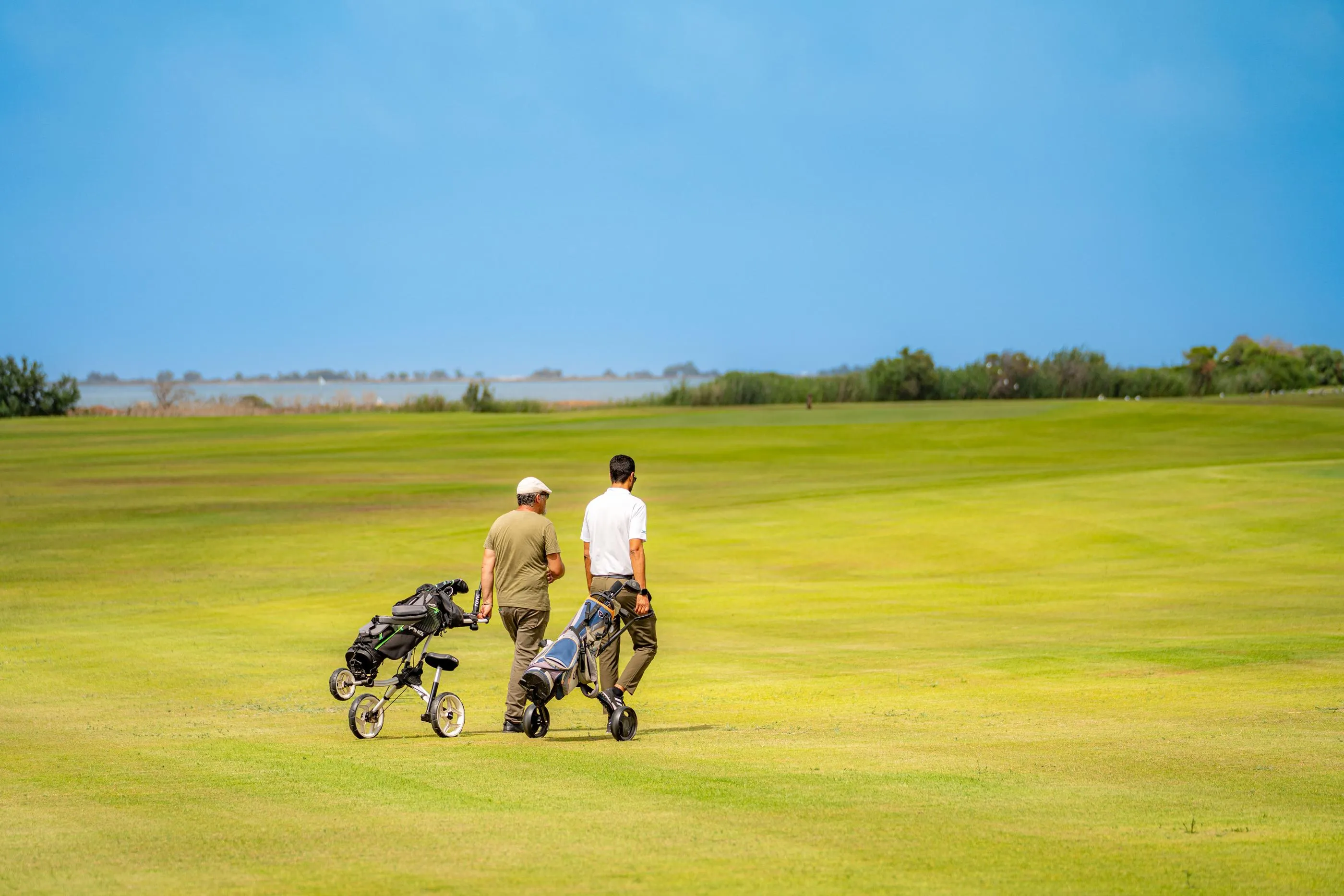 Deux personnes marchent sur un terrain de golf avec des chariots de clubs, sous un ciel dégagé