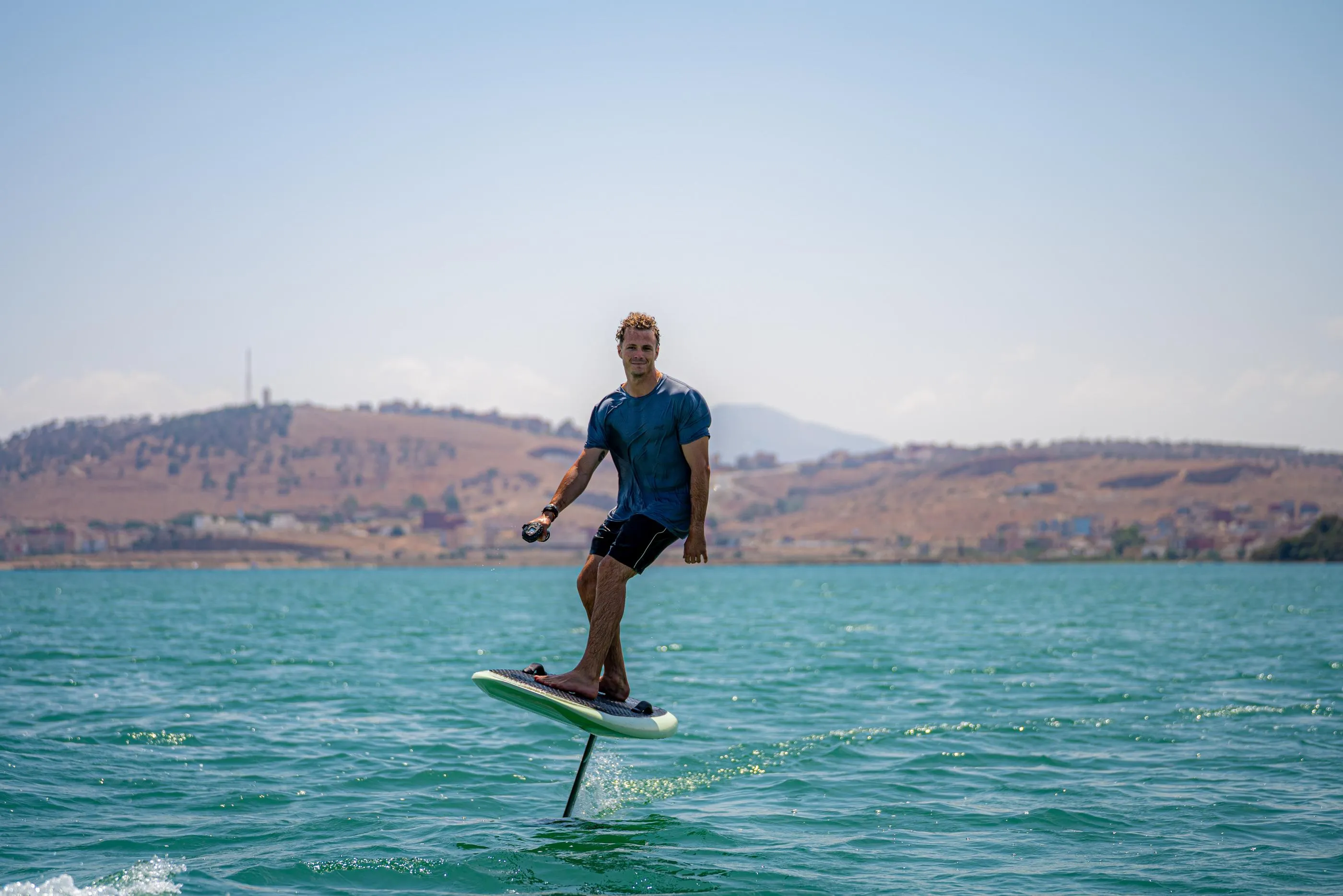 Un homme debout sur une planche de paddle dans une étendue d'eau avec des collines en arrière-plan