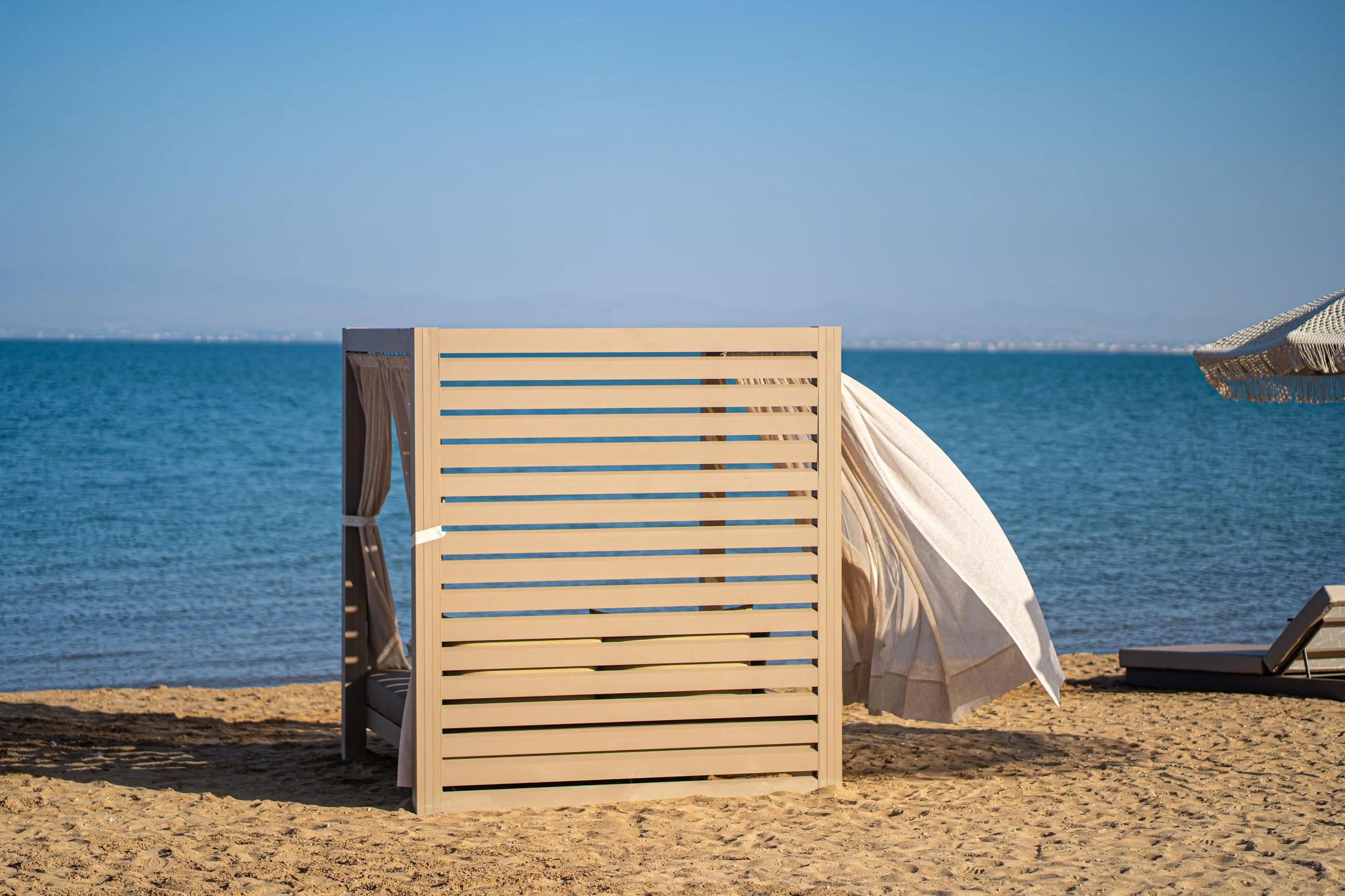 Cabane en bois sur une plage de sable avec une toile blanche et une vue sur la mer bleue