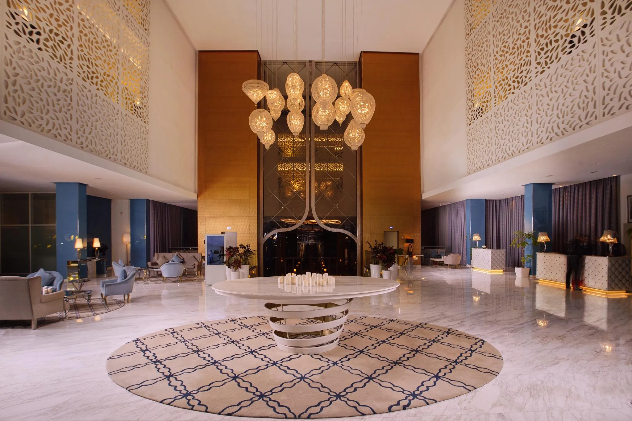 Lobby d'hôtel luxueux avec un grand lustre, des canapés, des tables basses et des murs décorés de motifs géométriques