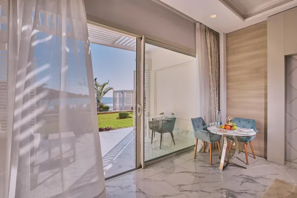 Une table avec des fruits et des verres est installée près d'une porte vitrée ouverte sur un balcon avec vue sur la mer