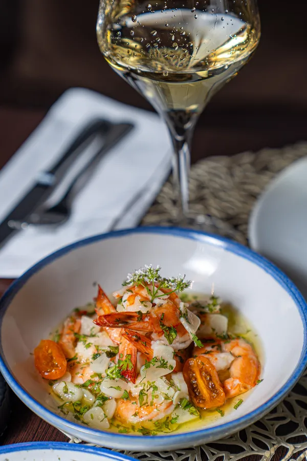 Un bol de crevettes grillées avec des tomates cerises et des oignons, accompagné d'un verre de vin blanc