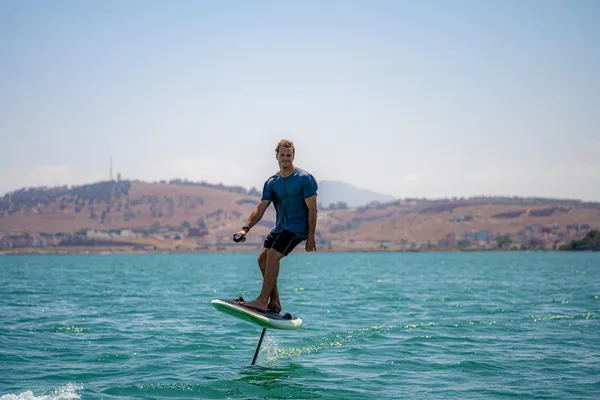 Un homme debout sur une planche de paddle dans une étendue d'eau avec des collines en arrière-plan