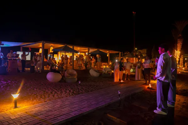 Un groupe de personnes se tient autour d'une structure éclairée sur une plage de nuit