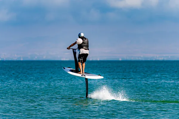 Un homme sur une planche de paddle électrique avance sur l'eau avec un jet d'eau derrière lui