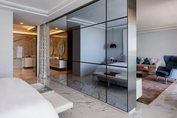 Intérieur moderne avec un miroir séparant une chambre à coucher et un salon, montrant des meubles blancs et un coin salon avec canapé et fauteuil
