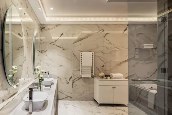 Salle de bain moderne avec double vasque, miroir rond, douche vitrée et murs en marbre beige