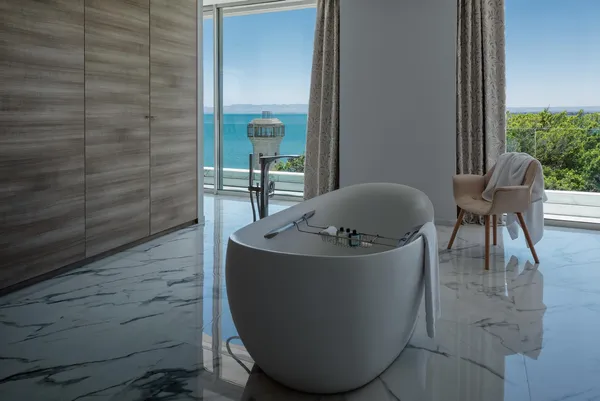Baignoire blanche avec des serviettes posées dessus, située dans une pièce avec vue sur la mer et un fauteuil recouvert d'une serviette