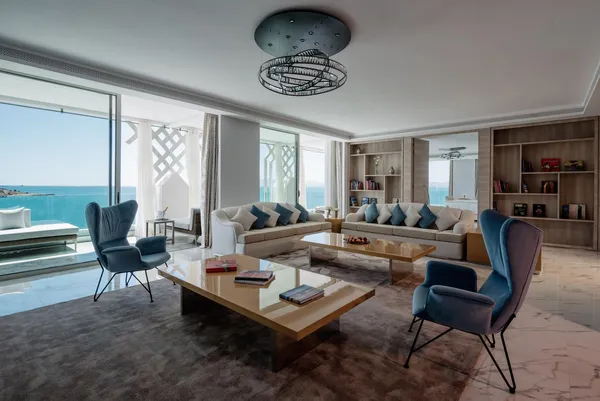 Salon moderne avec vue sur la mer, comprenant un canapé, des fauteuils, une table basse et des étagères remplies de livres